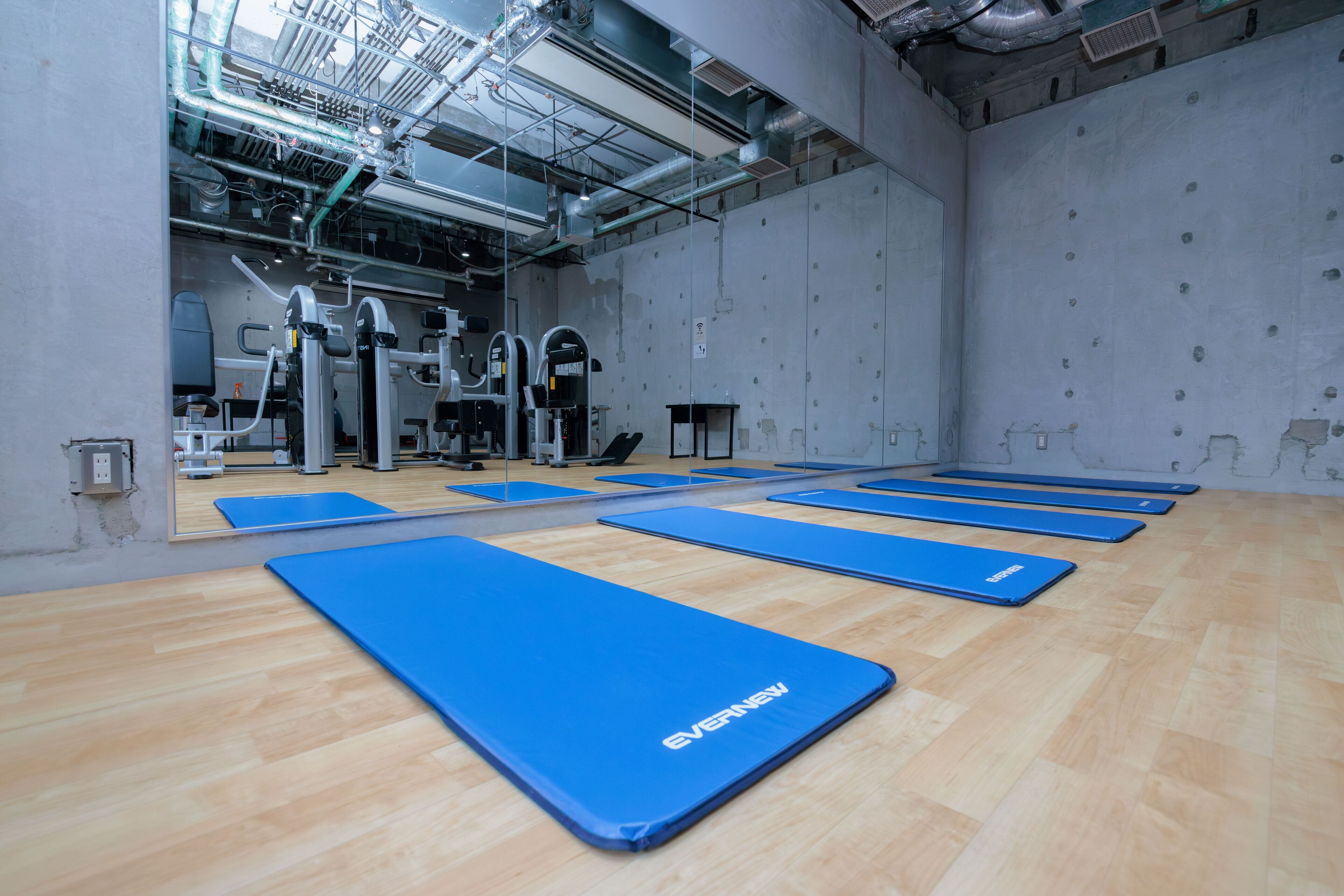 Un gimnasio con colchonetas azules, equipamiento de ejercicio y suelo de madera.