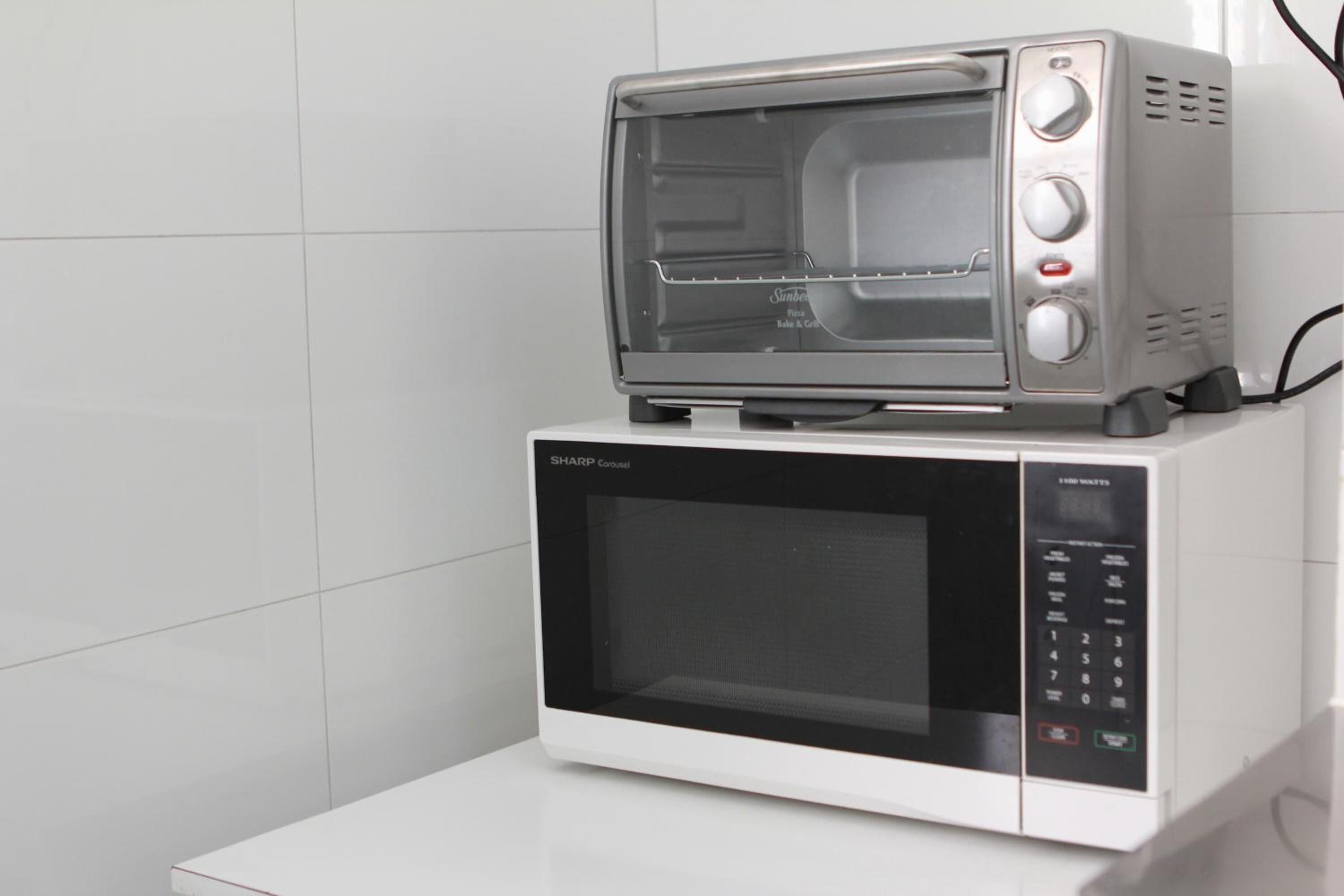 Un horno microondas con un tostador encima, ambos sobre una encimera blanca.