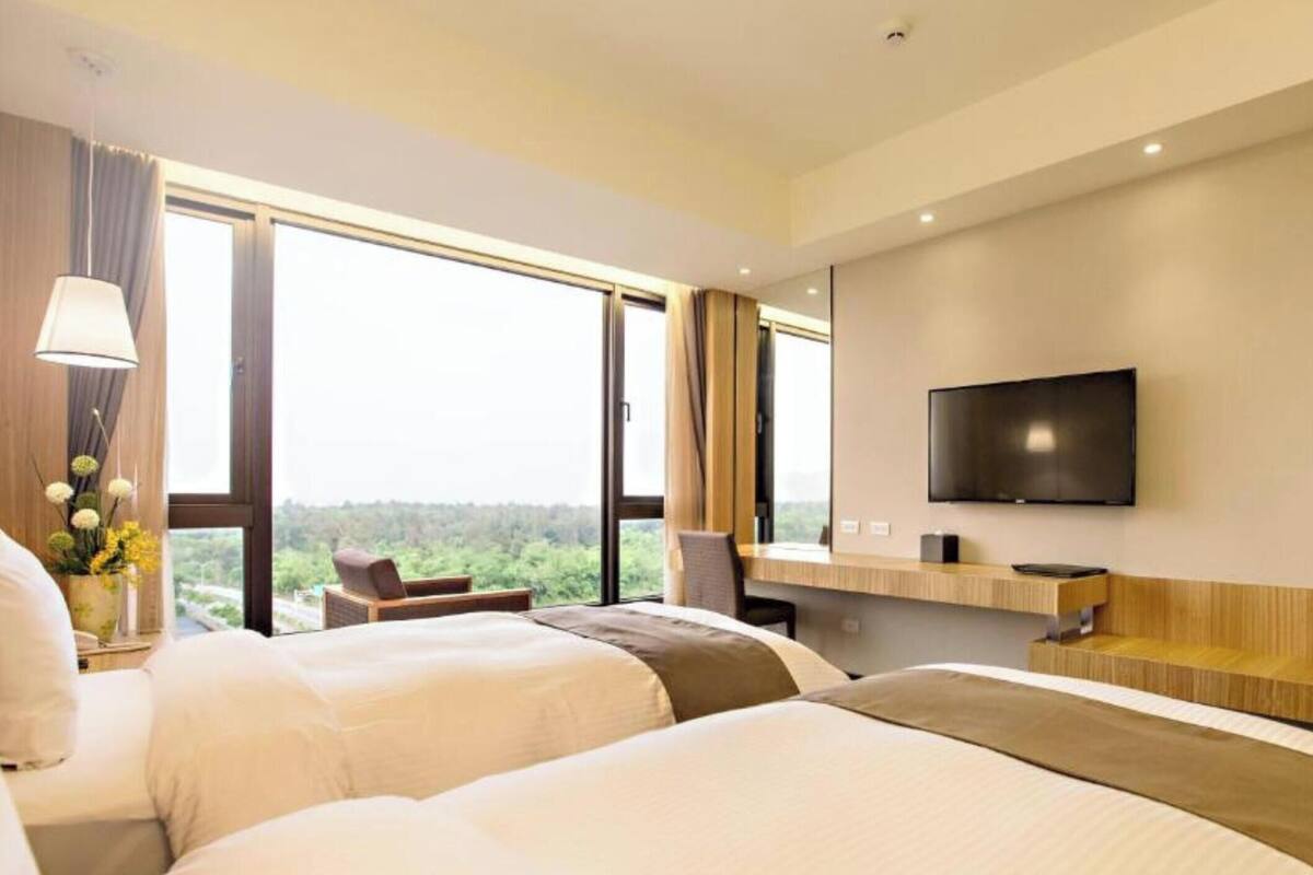 Habitació d'hotel amb dos llits, televisió i una finestra gran amb vistes.