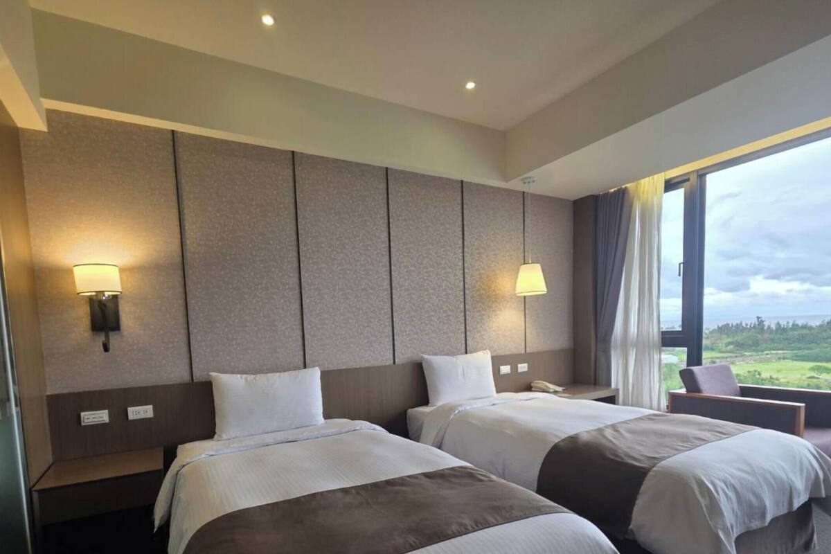 Habitació d'hotel amb dos llits, una finestra gran amb vistes i làmpades de paret.