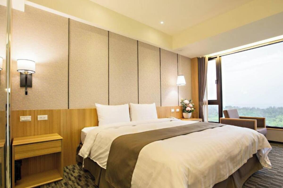 Habitació d'hotel amb un llit gran, taules de nit, una finestra amb vistes i una làmpada penjada a la paret.