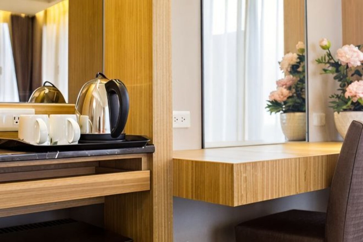 Una habitación de hotel moderna con un escritorio de madera, una tetera y un jarrón con flores.