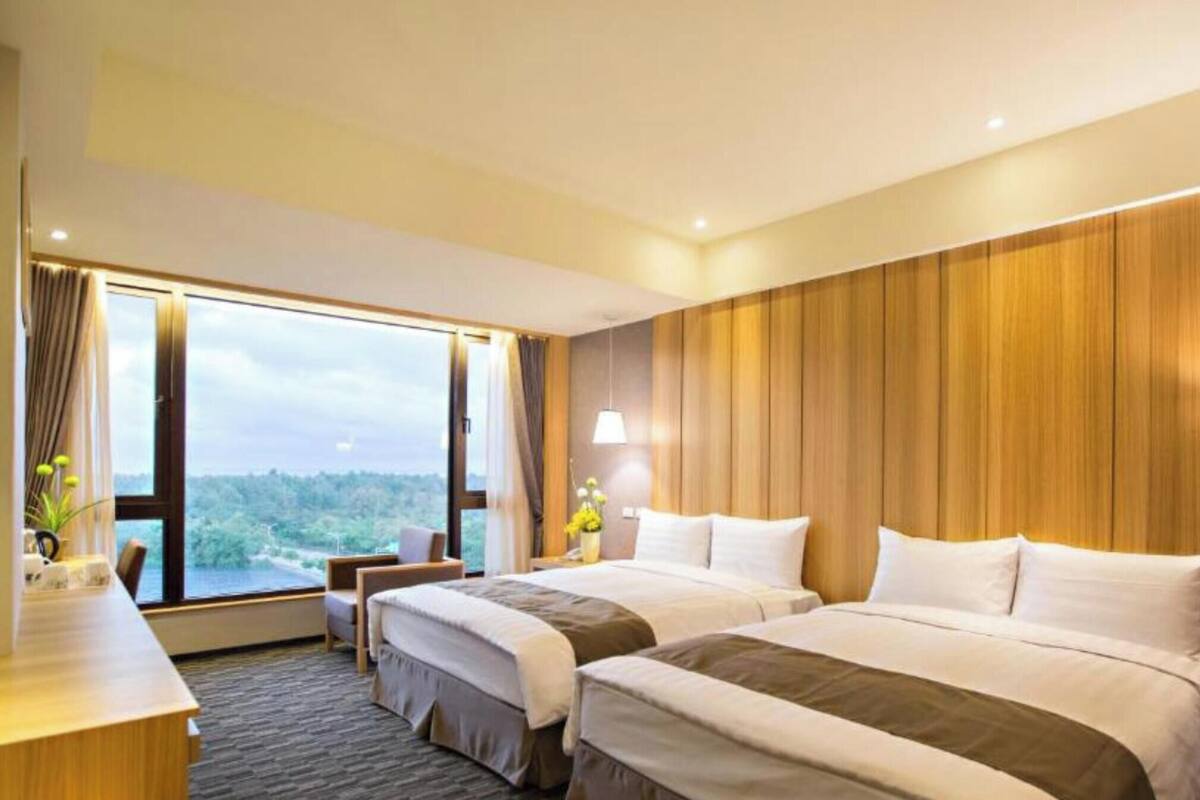 Habitació d'hotel amb dos llits, una taula de treball i una finestra gran amb vistes.