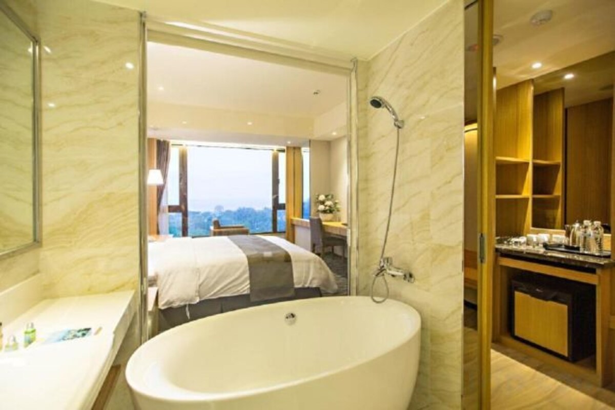 Un baño moderno con una bañera grande, ducha y vista a un dormitorio con cama y escritorio.