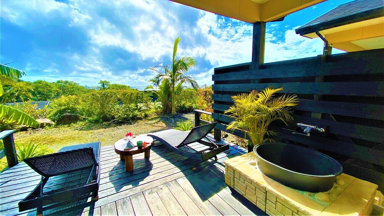 Terraza de madera con sillones, una mesa y un jacuzzi.