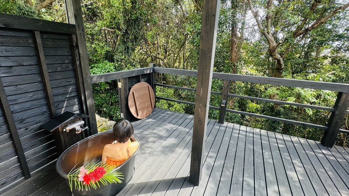 Una terraza de madera con una bañera, un banco de madera y una barandilla de metal.