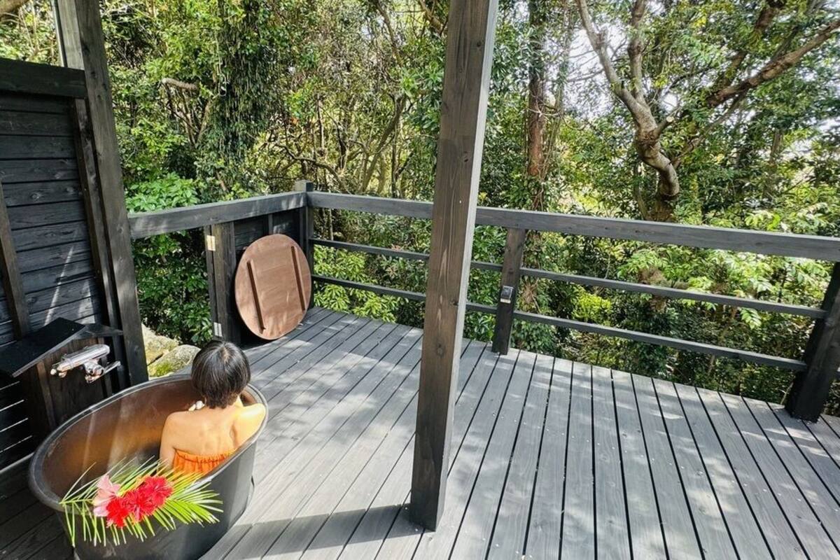 A wooden deck with a bathtub, a wooden bench, and a metal railing.