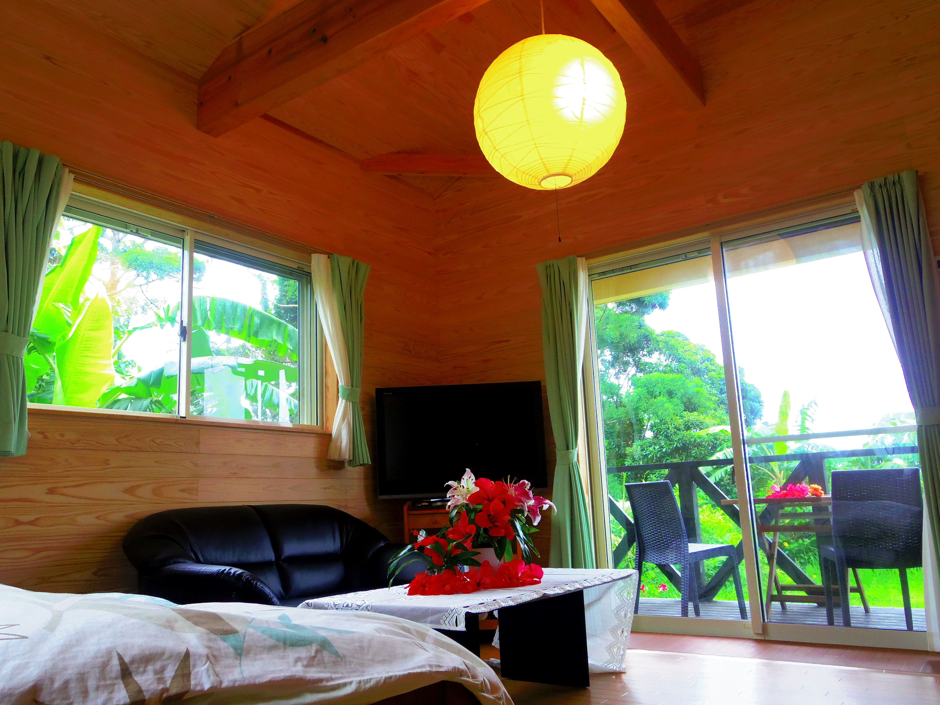 Une chambre avec un lit, une télévision, une table ornée d’un vase de fleurs et un balcon avec des chaises.