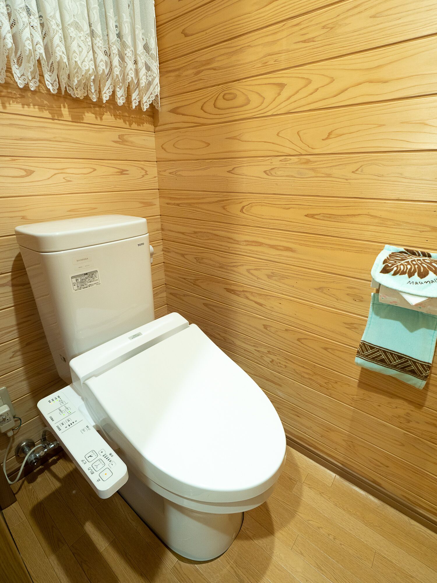 A toilet with a control panel, a wooden wall, and a towel with a leaf pattern.