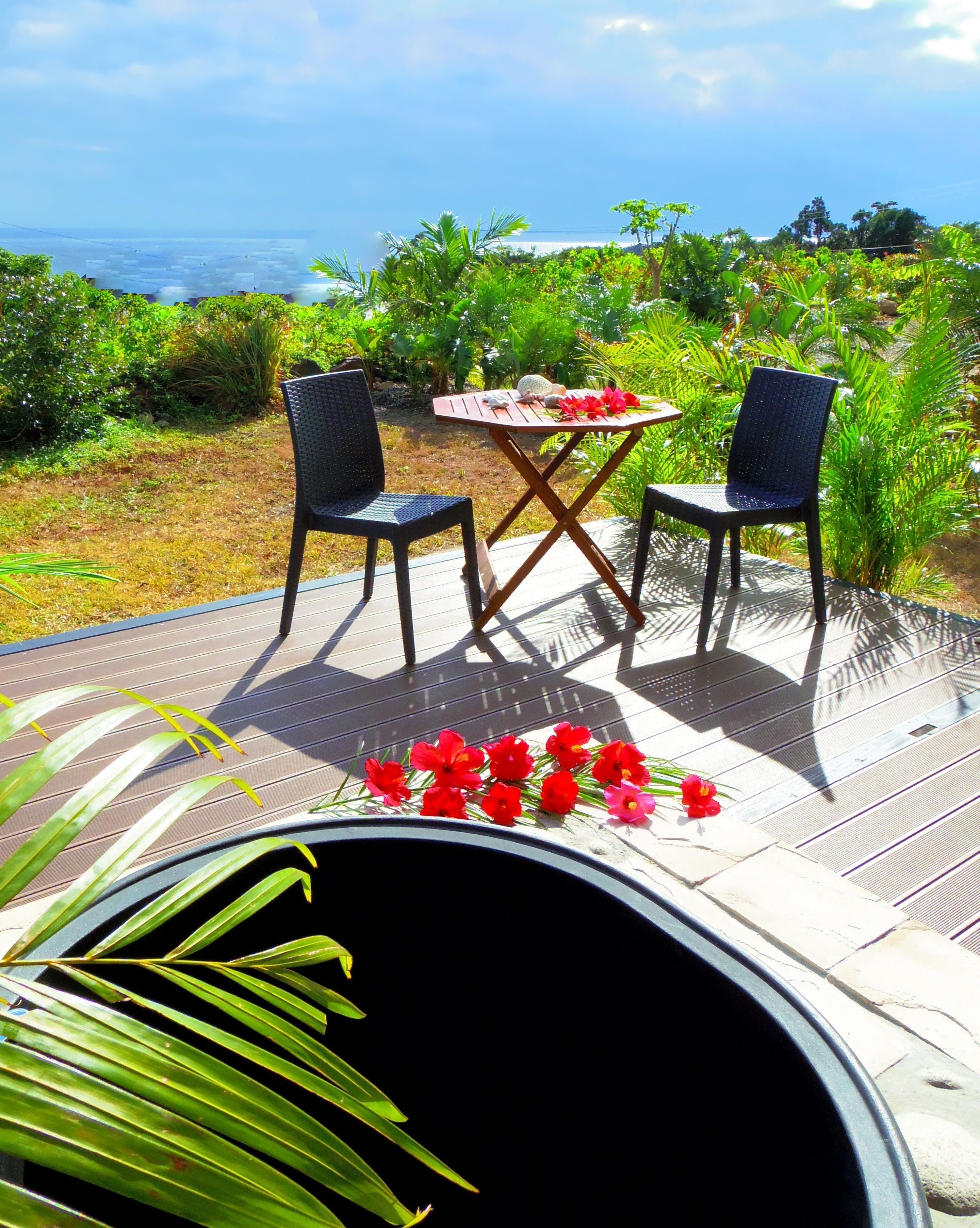 Un área de estar al aire libre con dos sillas y una mesa, rodeada de exuberante vegetación y vistas al océano.