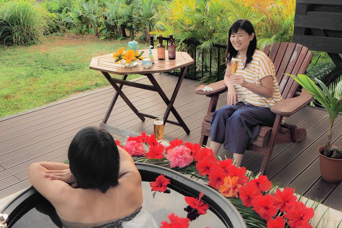 A person sitting on a chair with a table in front of them, holding a glass.