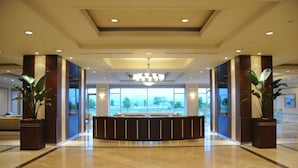 A spacious lobby with a central reception desk, large windows, and potted plants. - Hotel Arrowle (Kaga)