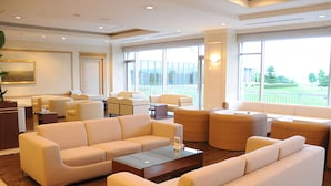 A spacious hotel lobby with modern furniture, large windows offering a view of the outdoors, and a reception desk. - Hotel Arrowle (Kaga)