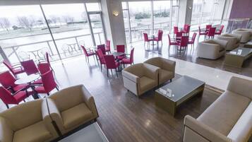 A spacious indoor area with multiple seating arrangements, including sofas and chairs, and large windows providing a view of the outdoors.
