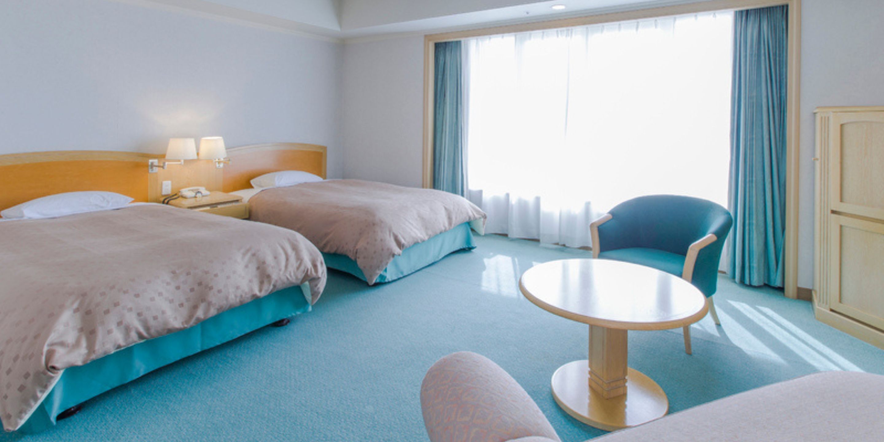 A hotel room with two beds, a round table, a chair, and a wardrobe.