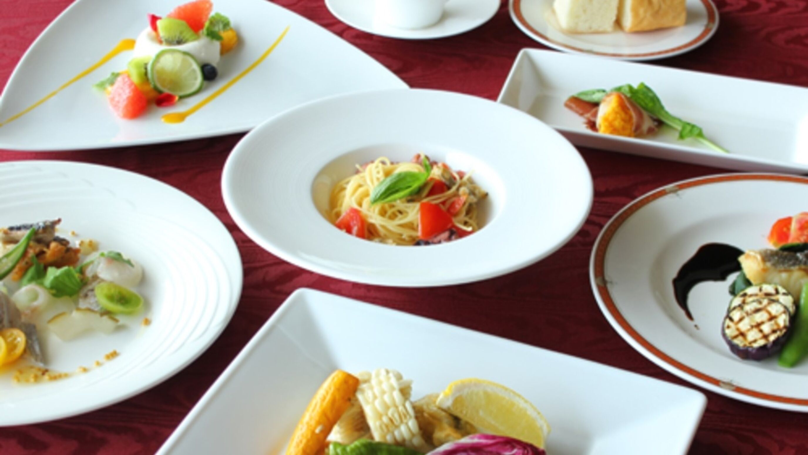Une variété de plats servis dans des assiettes blanches, sur une table recouverte d’une nappe rouge.