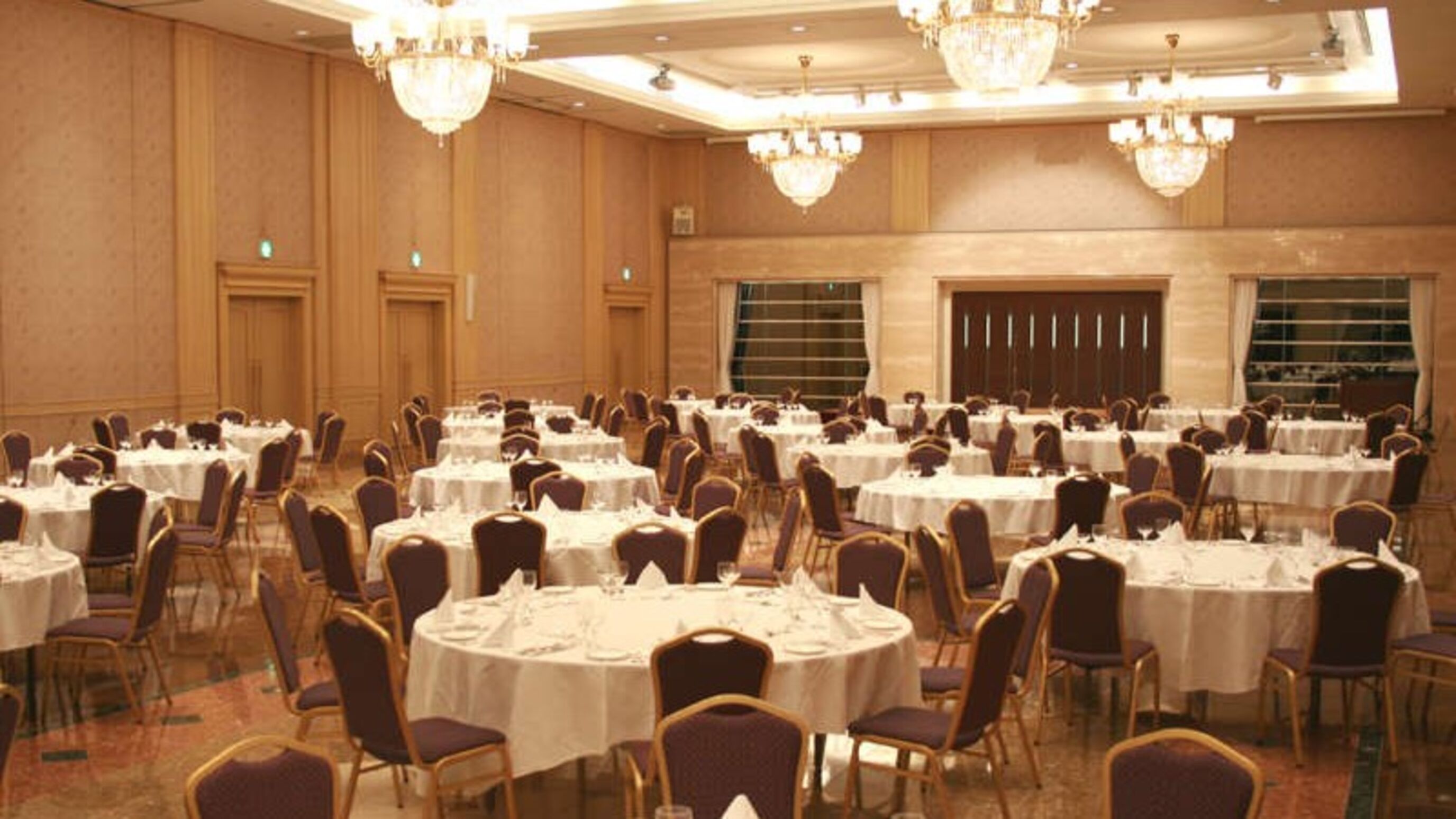 A banquet hall with round tables and chairs, chandeliers, and wooden paneling.