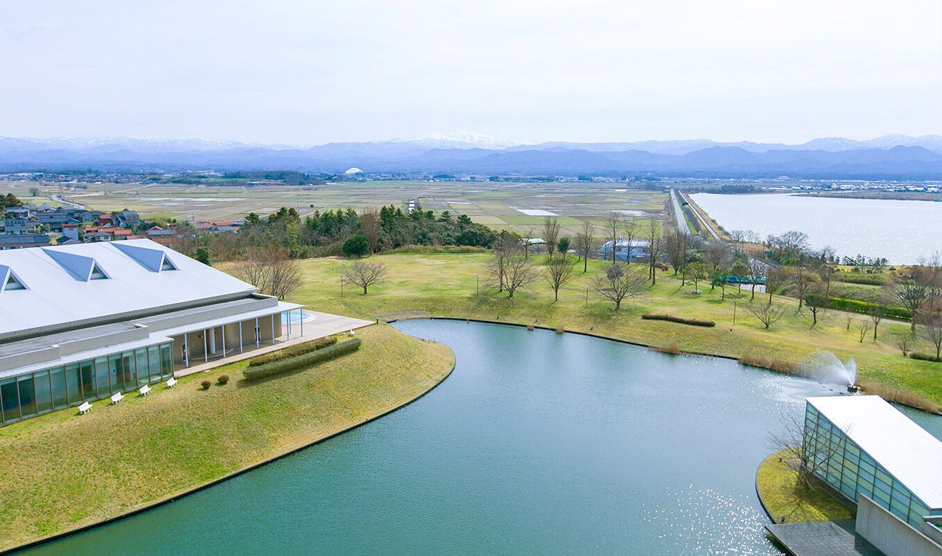 A modern building with a large glass facade, a curved water feature, and a view of distant mountains.