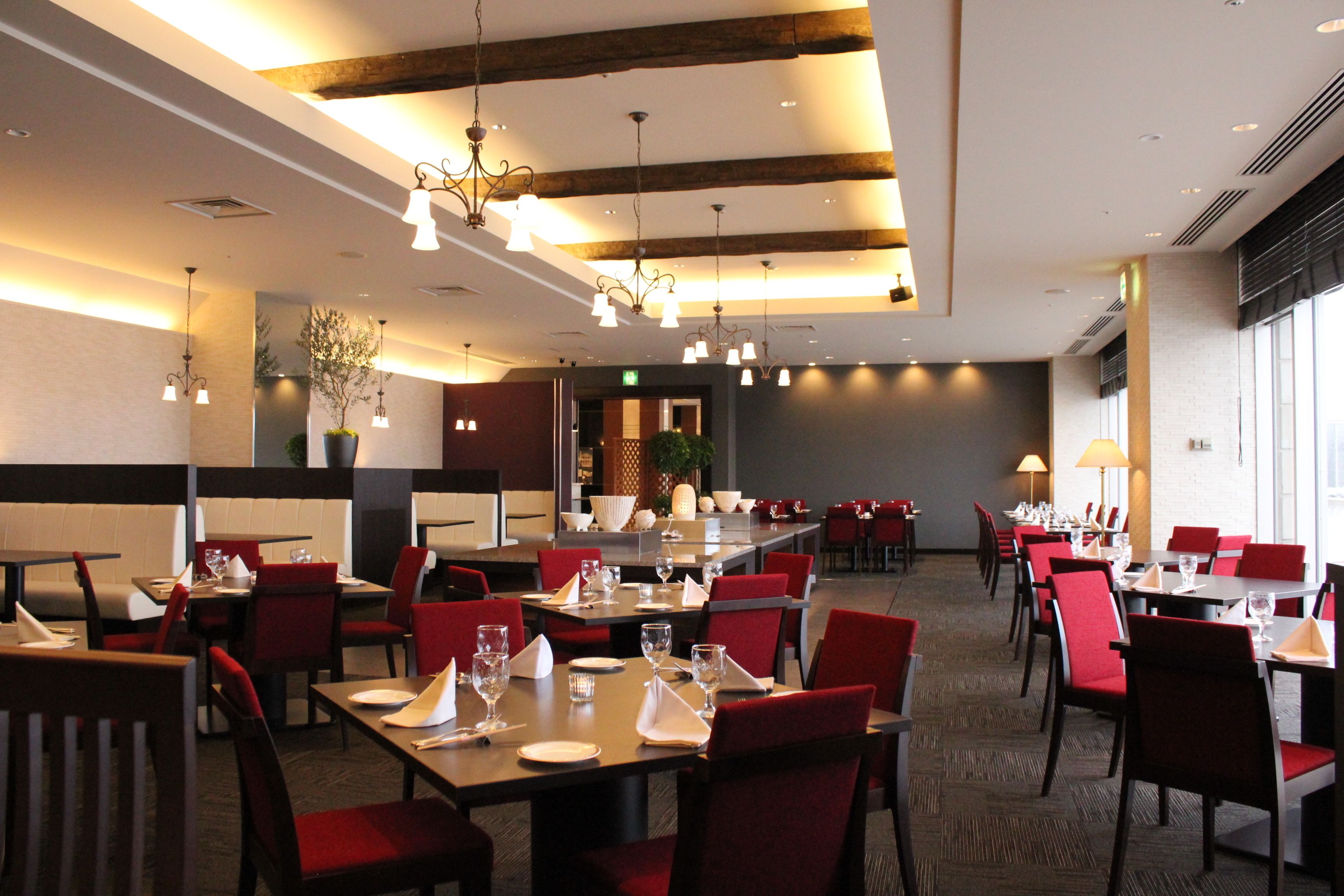 Un restaurante con sillas y mesas rojas, vigas de madera en el techo y lámparas colgantes.