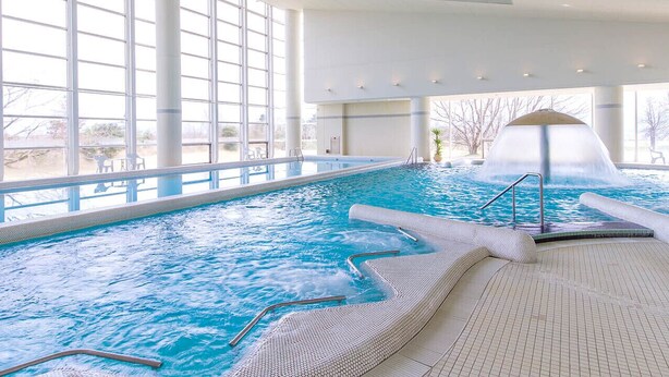 An indoor swimming pool with clear water, a hot tub, and a waterfall feature. - Hotel Arrowle (Kaga)