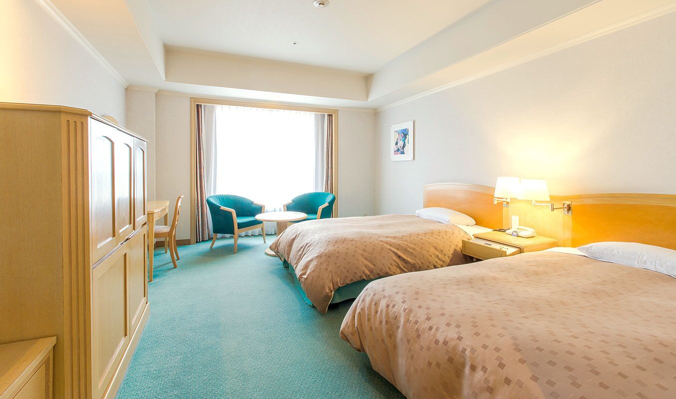 A hotel room with two beds, a desk, a chair, and a window with curtains.