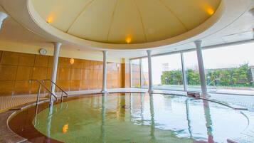 An indoor swimming pool with a tiled floor, a glass wall, and a ceiling with lights.