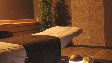 Two single beds with white linens and dark blankets, a potted plant, and a simple design.