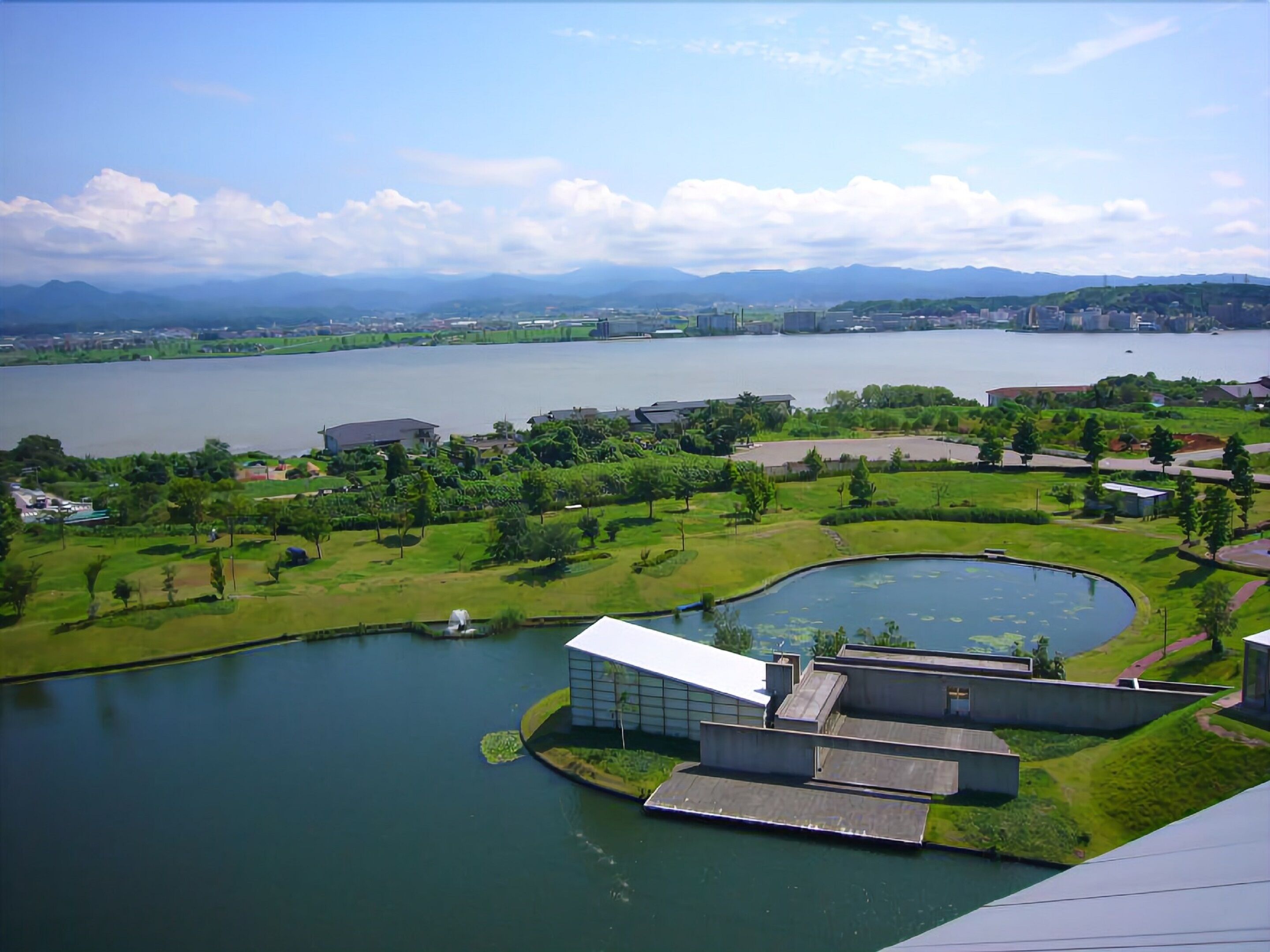 A lakeside view with a modern building featuring a flat roof and a small pond.