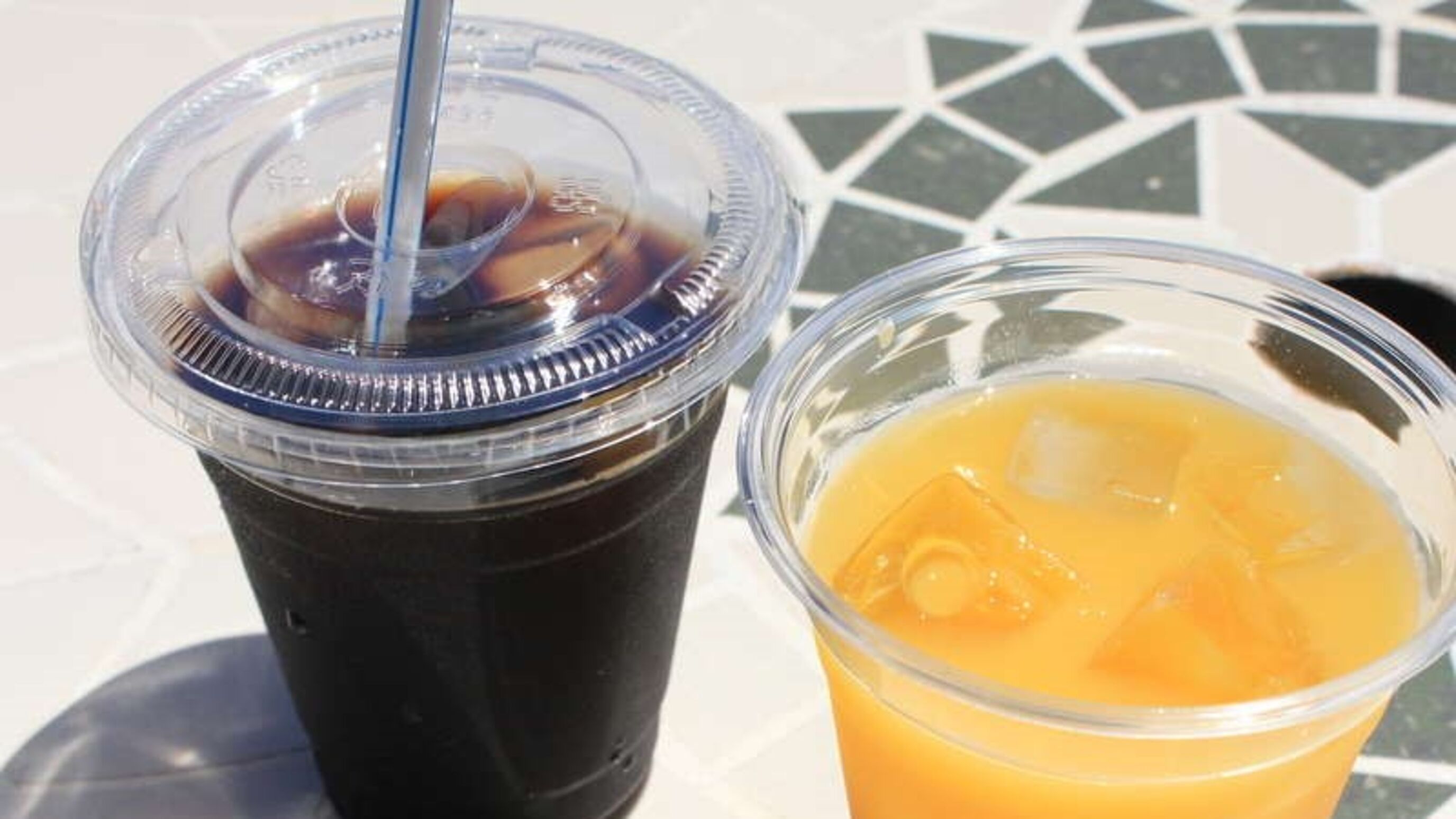 Two plastic cups, one with iced coffee and the other with iced tea, on a tiled surface.