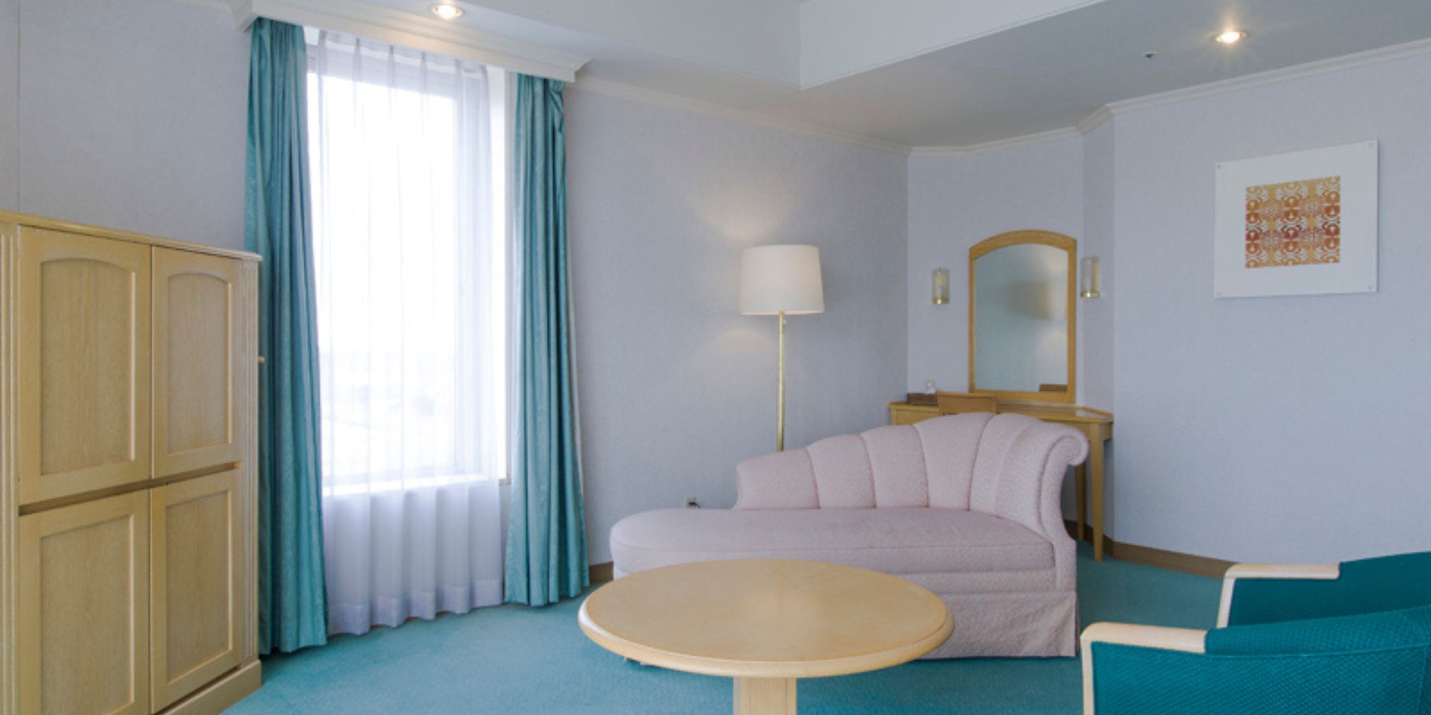 A hotel room with a bed, a round table, a sofa, a wardrobe, a mirror, and a window with curtains.