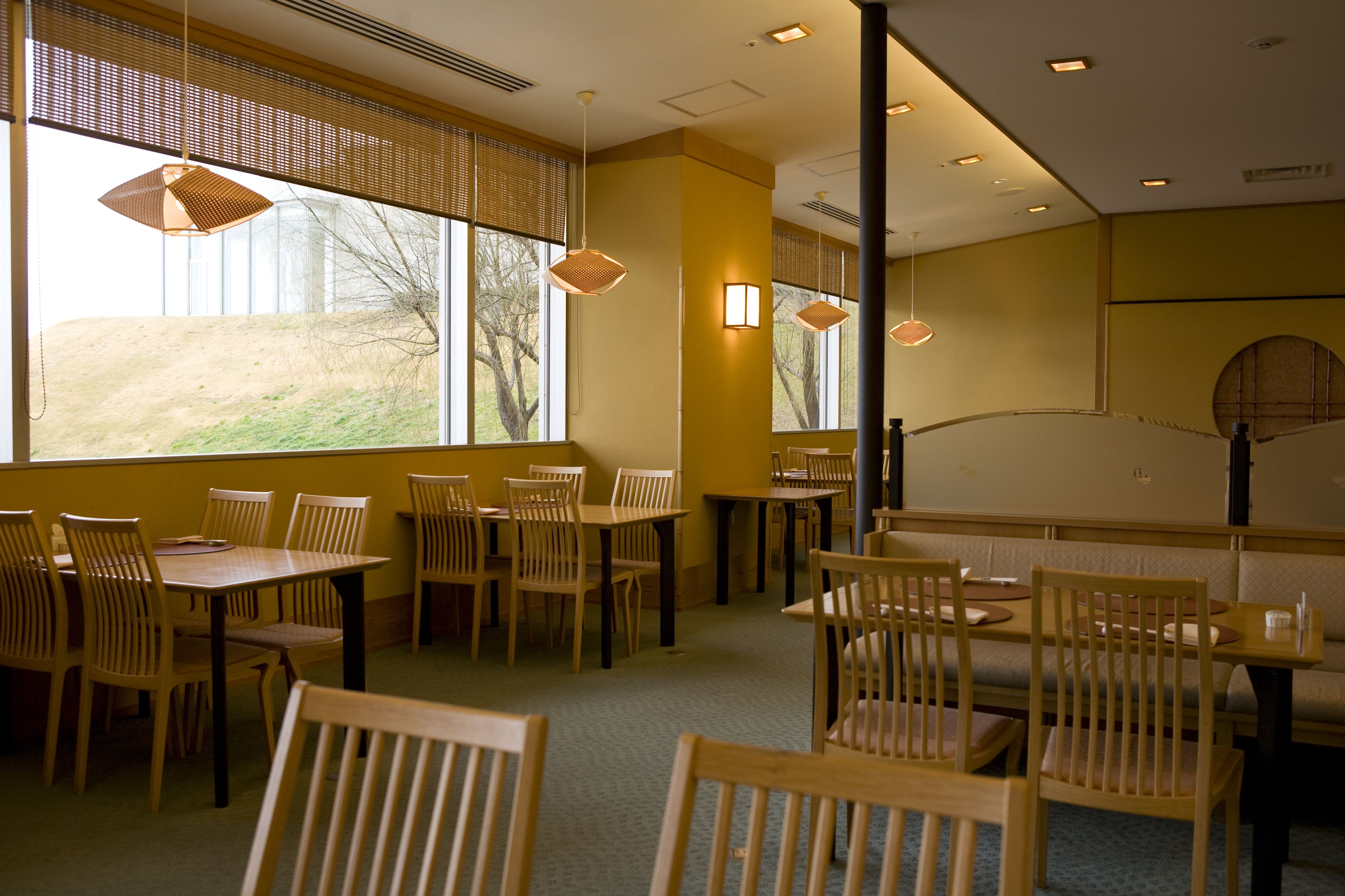 A restaurant with wooden furniture, large windows, and pendant lighting.