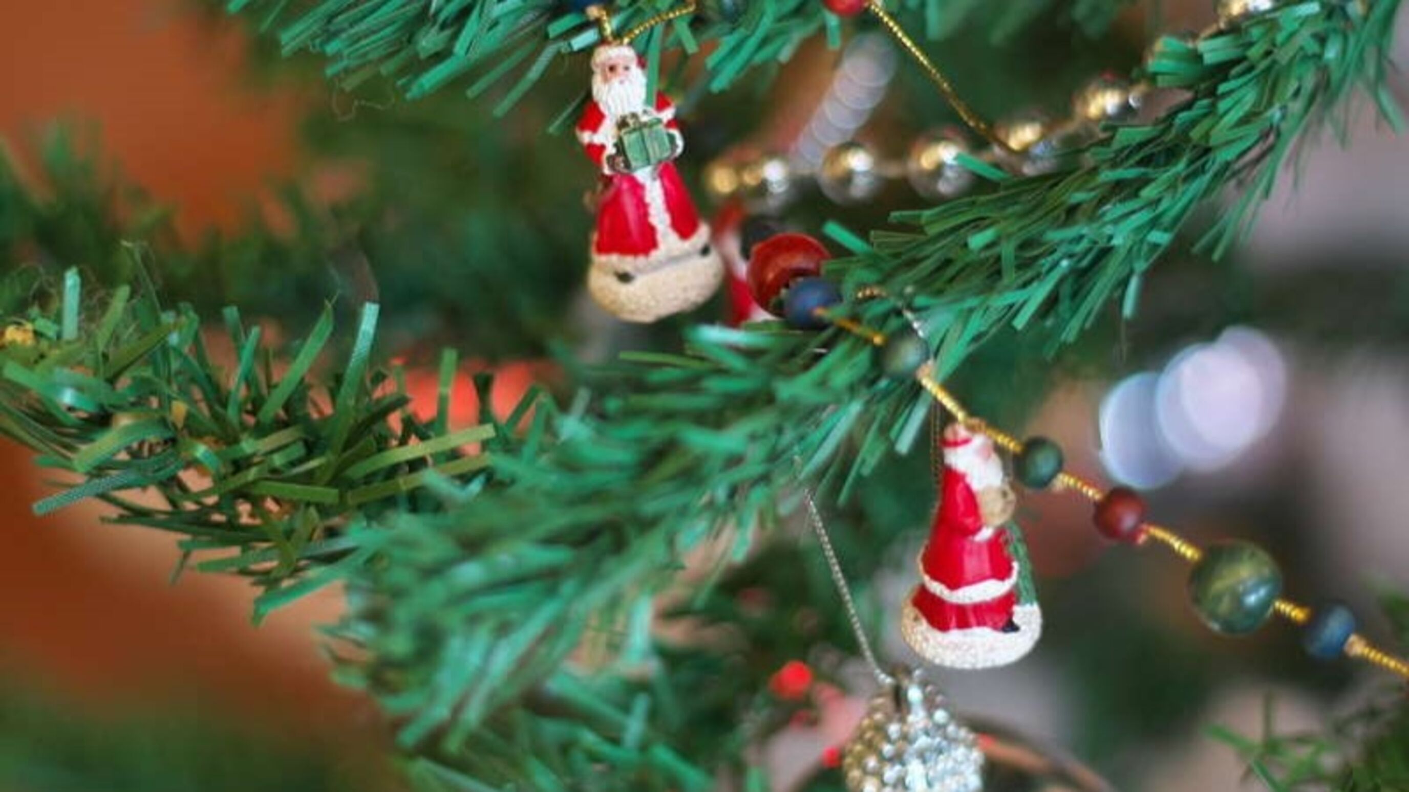 A close-up of a Christmas tree with ornaments, including a Santa Claus figure and a beaded ornament.