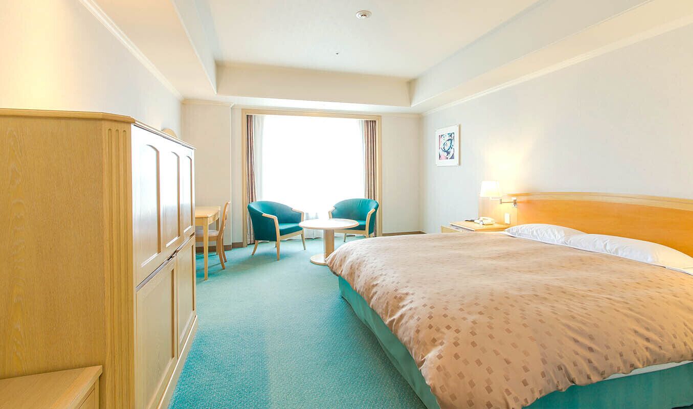 A hotel room with a bed, a desk, two chairs, a wardrobe, and a window.