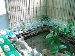 Un petit jardin clos, avec un bassin en pierre, entouré de rochers et de plantes.