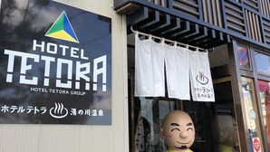 Entrada de hotel con un letrero del Hotel Tetora Group, una gran figura de mascota y una fachada de edificio moderna.