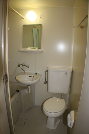 Une petite salle de bain compacte avec un lavabo blanc, des toilettes et un miroir au-dessus du lavabo.