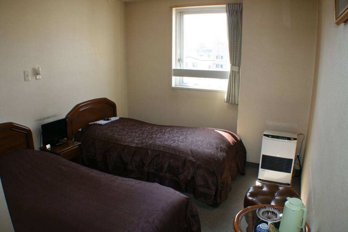 Une chambre avec deux lits, une petite table avec une bouilloire et une fenêtre avec des rideaux.