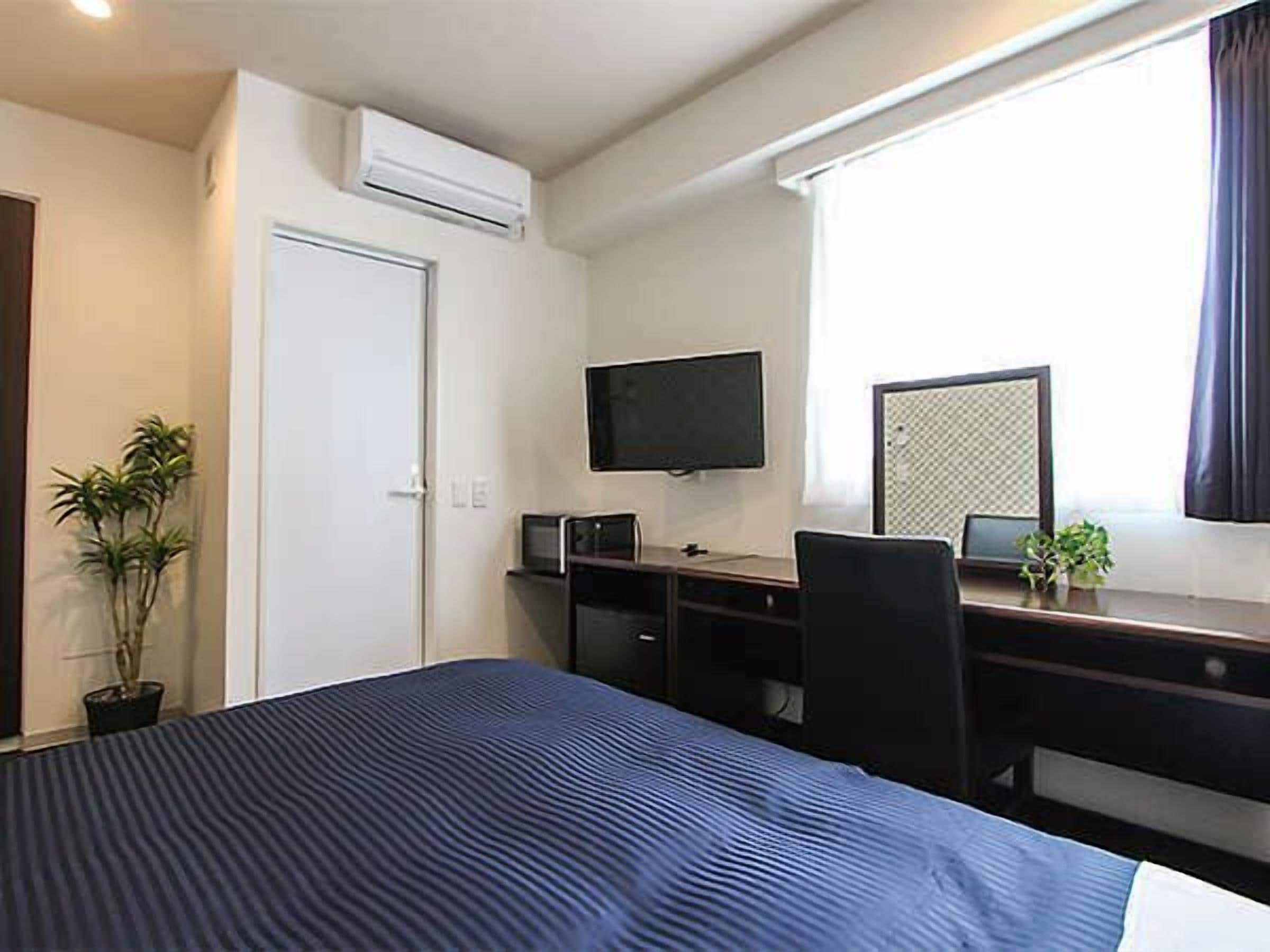 Habitación de hotel con cama, escritorio con computadora, televisor y ventana con cortinas.