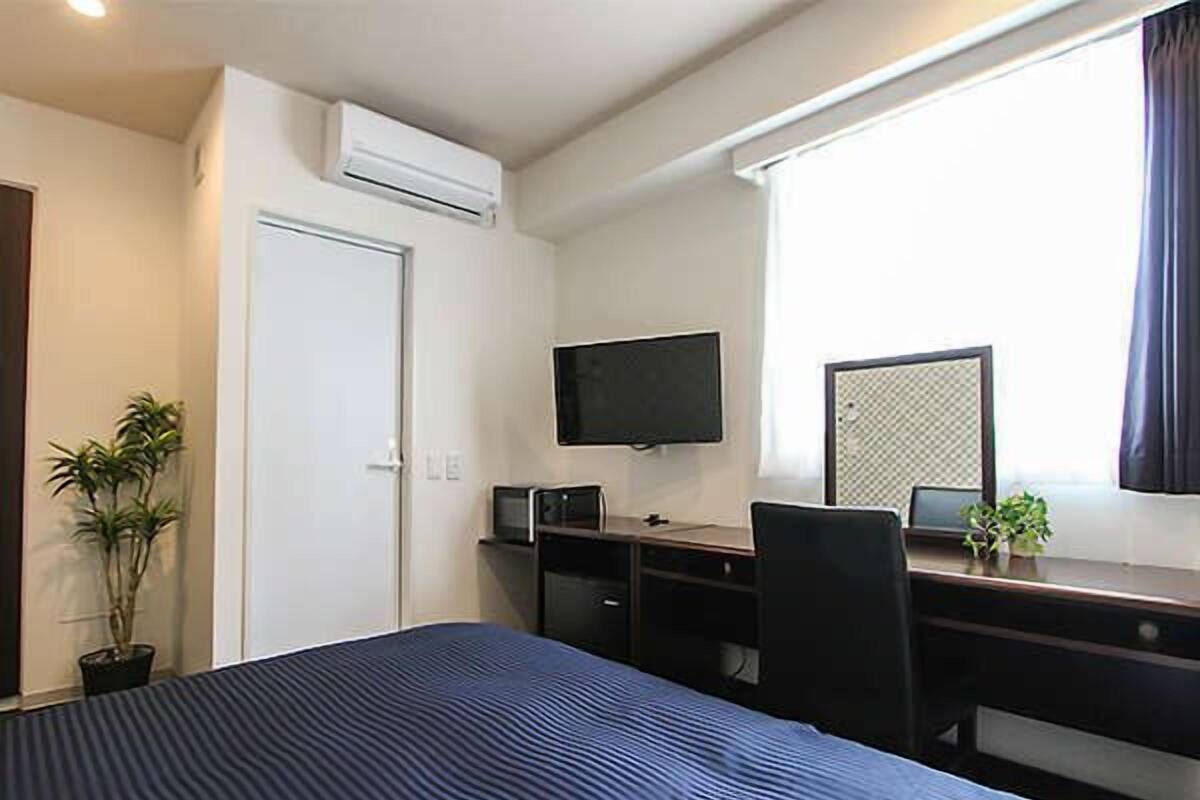 Een hotelkamer met een bed, een bureau met een computer, een televisie en een raam met gordijnen.