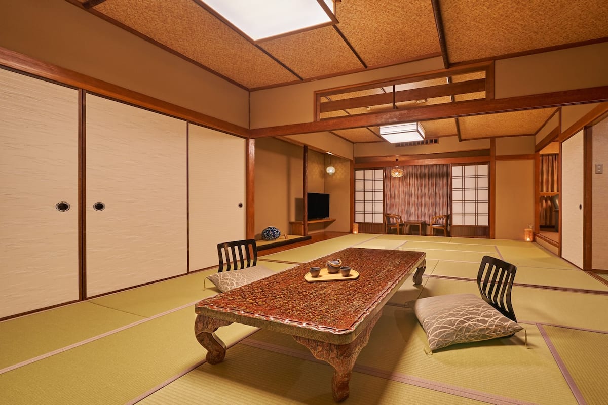 A traditional tatami room with a low table, chairs, and a television.