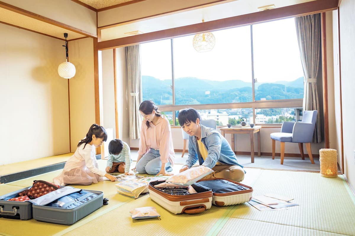 A tatami mat room with traditional Japanese furniture, a large window with a view of mountains, and a hanging light fixture.