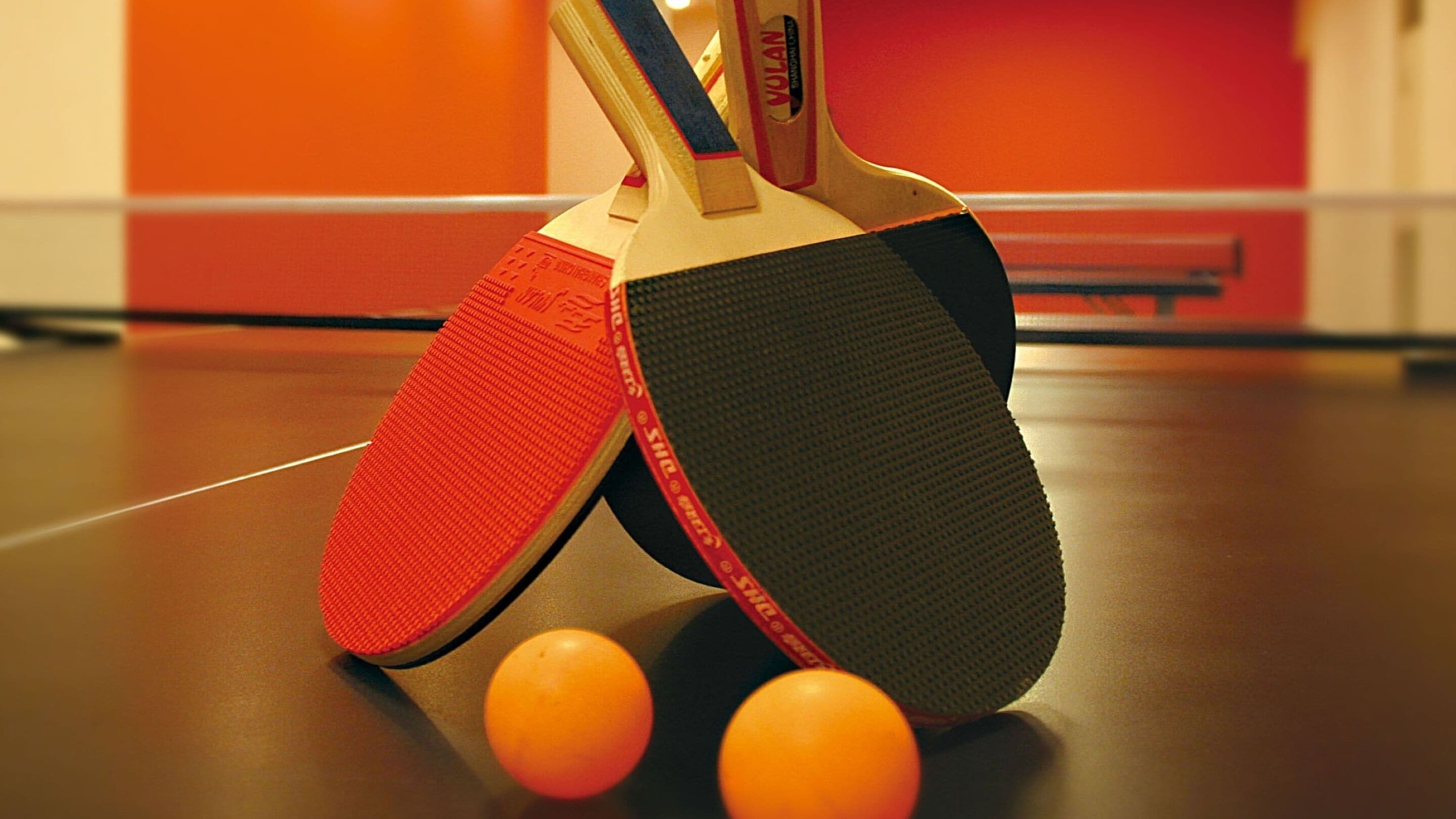 Two table tennis paddles and two orange balls on a table.