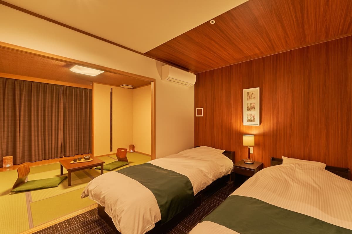 A hotel room with two beds, a wooden ceiling, a small table with a chair, and a picture on the wall.