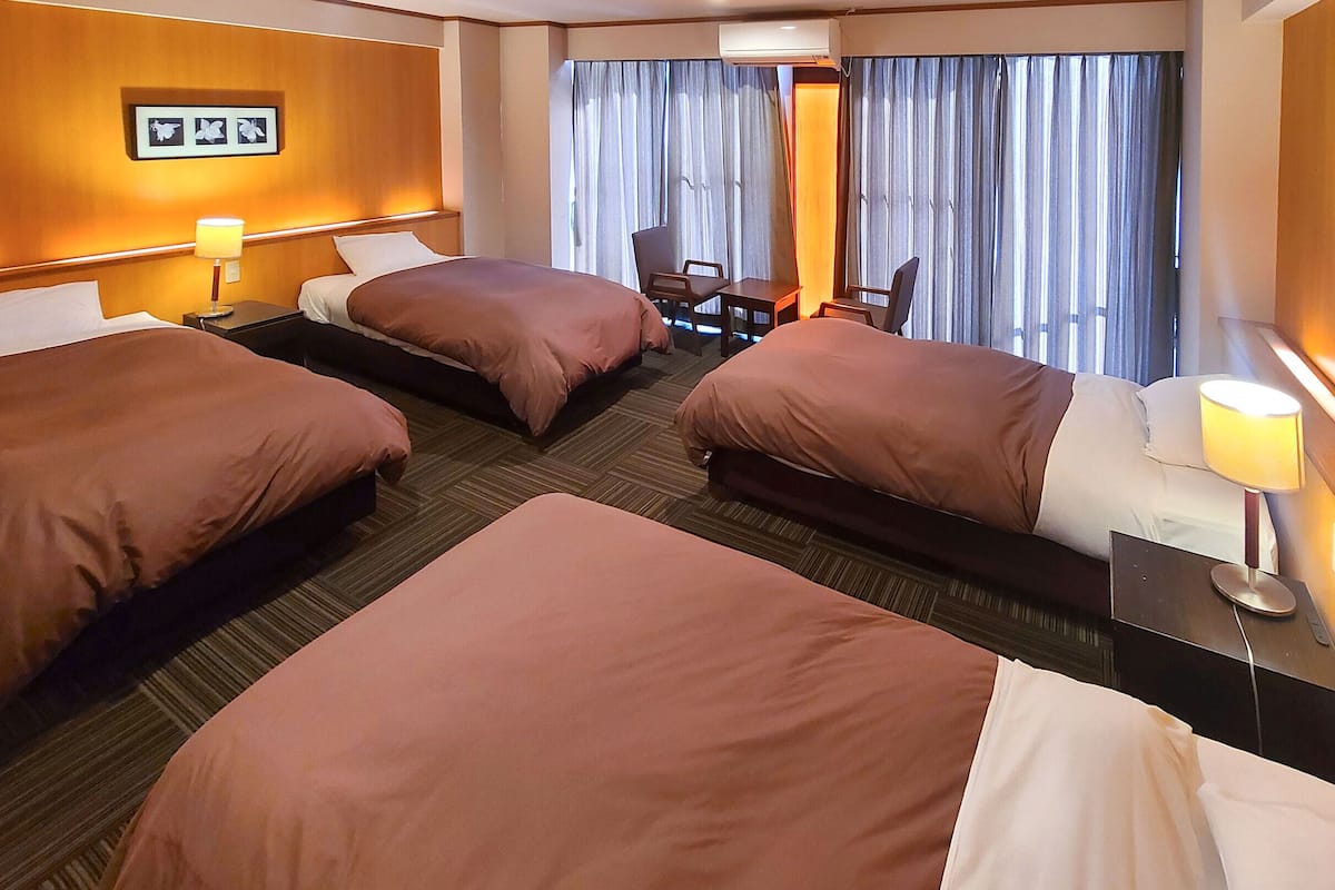 A hotel room with three beds, a desk, and a chair.
