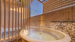 A hot spring bath area with a stone basin, wooden fence, and a bamboo wall.