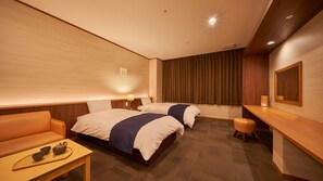 Ein Hotelzimmer mit zwei Betten, einer Schlafcouch, einem kleinen Tisch mit Teeservice und einem Schreibtisch mit Lampe.