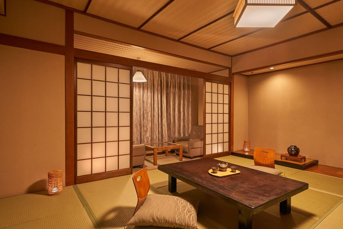 A traditional Japanese-style room with tatami flooring, a low table, chairs, and sliding doors.