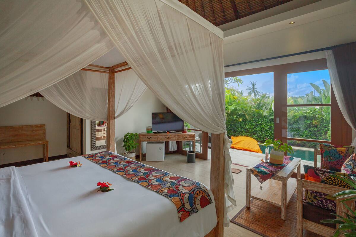 A bedroom with a bed, a desk, a television, and a view of greenery outside.