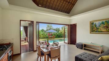 A spacious living area with a dining table set for four, a sofa, and a view of a swimming pool.