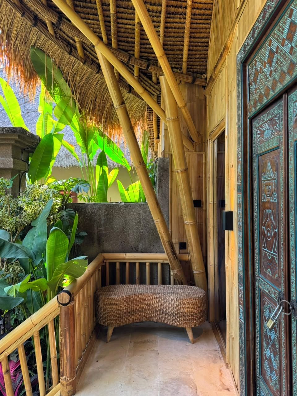 A narrow corridor with a woven bench, bamboo structures, and a decorative door.